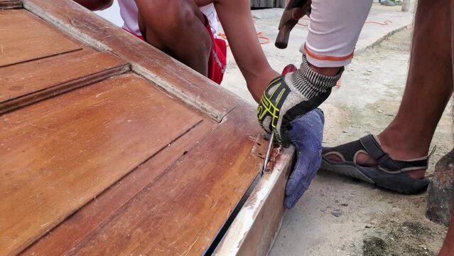 man repair wooden door, remove rusty hinge with hammer and screwdriver, handcraft work
