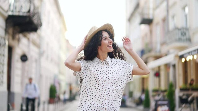 Excited young attractive pretty woman tourist in a hat walking on a city street. old town Curly haired hispanic happy lady is joyful enjoying the trip leisure time Concept travel, journey lifestyle