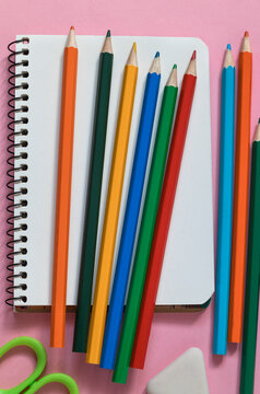Notebook, colorful pencils crayons on a pink background. Back to school concept.