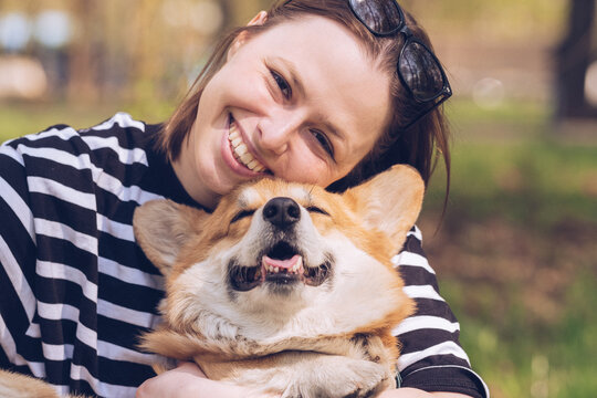 Portrait of a caucasian woman in a striped T-shirt hugs her corgi dog in a park