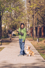 Fototapeta premium Portrait of a caucasian woman in green sweater and with corgi dog in a park