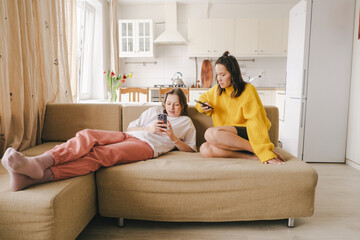Two cheerful girls holding mobile phones while sitting at home on a couch
