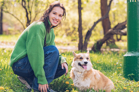Portrait of a caucasian woman in green sweater and with corgi dog in a park