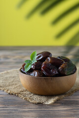 Light wooden bowl with dried dates on a canvas napkin. Light wooden table. Yellow background