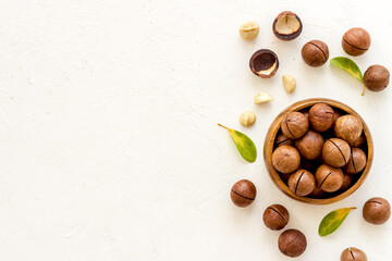 Shelled macadamia nuts with green leaves. Healthy snack background - obrazy, fototapety, plakaty