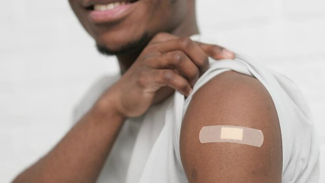 vaccinated African American man showing arm with medical plaster patch Plaster On Shoulder, black male after getting vaccine dose against covid virus, Healthcare immunization, coronavirus vaccination