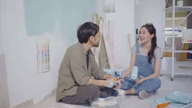 Asian couple talking chatting while taking a break from painting the walls of their house.