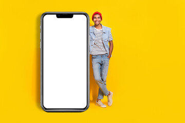 Fototapeta na wymiar Full length photo of pretty positive man wear jeans outfit holding device empty space isolated yellow color background