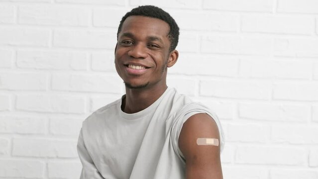 vaccinated African American man showing arm with medical plaster patch Plaster On Shoulder, black male after getting vaccine dose against covid virus, Healthcare immunization, coronavirus vaccination