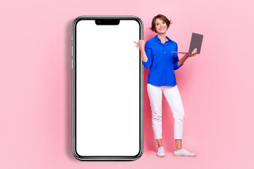 Full body length size photo of positive entrepreneur beautiful woman hold netbook directing finger phone display isolated on pink color background