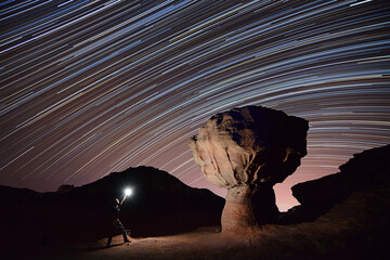 man standing near a rock mushroom and lighting it during the night with startrails in the back ground in Timna park near Eilat - Israel  - obrazy, fototapety, plakaty