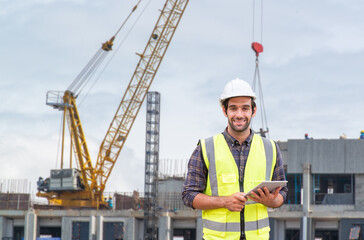Business, building, industry, technology, and people concept - jovial builder in hardhat over group of workers at construction site while using tablet computer