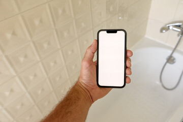 Smartphone mockup in bathroom, man holding mobile phone with blank touch screen over the bathtub