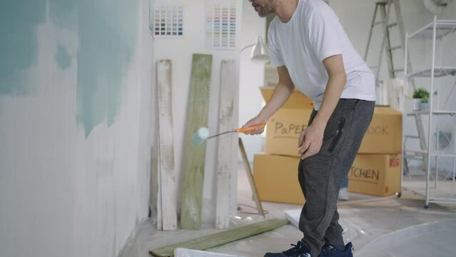 Young Asian couple repairing and painting the wall with blue paint using a roller during renovation in their new apartment.