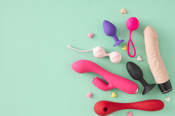 Erotic pleasure toy concepts for adults. Top view flat lay of colorful vibrators, dildo, anal plugs, vaginal balls, hearts on turquoise background with blank space for message or promo