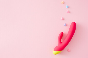 Sexual pleasure toy subject. Top view flat lay of dual vibrator, colorful hearts on pastel pink...