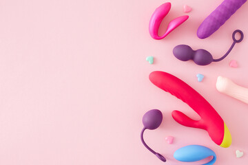 Concept of adult toys for erotic indulgence. Top view arrangement of vibrator, vaginal balls, massager for the clitoris and colorful hearts on pastel pink background with empty space for text or ad