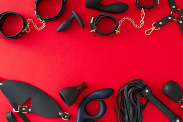 Ignite your desires with BDSM erotic toys. Top view composition of cuffs, leather mask, whip, vibrator, anal and vaginal plugs on red background with blank space for promo or text © Goncharuk film