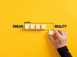 Transition of dreams into reality. Realizing the dreams. Hand places a wooden cube to the loading bar with the words dream and reality. - Powered by Adobe