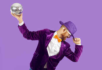 Overjoyed man performer or entertainer in party suit hold glitter disco ball dancing on purple...