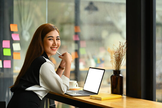 Image of successful startup business founder sitting in modern office with laptop and smiling at camera