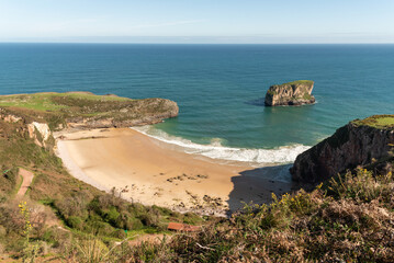 Fototapeta na wymiar Panoramic aerial view of the golden sandy beach and turquoise water of the tourist town of Andrin next to impressive cliffs on the coast of Asturias on a sunny summer day.