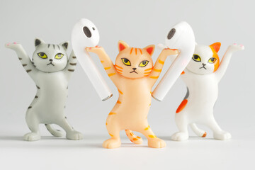 Fototapeta premium Funny toy cats advertise white wireless tws headphones. Unusual stand for tws headphones. Photo. Selective focus.