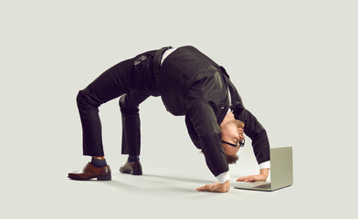Extravagant curious businessman standing in bridge position looking at laptop screen on gray...