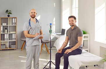 Happy male nurse together with patient. Portrait of young man sitting on medical bed and getting...