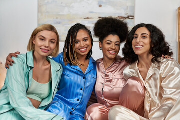 Portrait of positive african american women hugging multiethnic girlfriends in colorful pajama and...