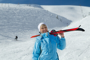 Female skier holding ski; blue jacket; horizontal orientation - obrazy, fototapety, plakaty