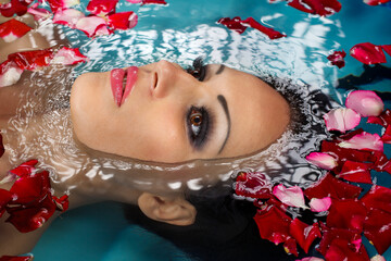 Face of pretty woman floating in swimming pool with petals of rose