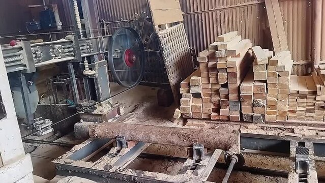A closeup of a band saw machine cutting lumber moving on rails at a sawmill