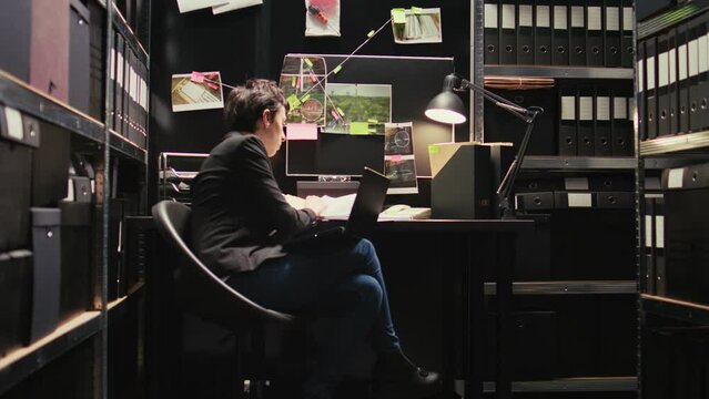 Criminologist reading classified records, using laptop to uncover new case details in police agency incident room. Woman law enforcement officer conducting criminal investigation with evidence.