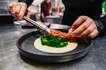 chef hand cooking salmon steak with broccoli and salad on restaurant kitchen