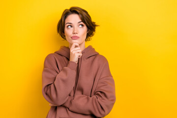 Photo of minded intelligent woman with short hairdo wear brown hoodie thoughtfully look empty space isolated on yellow color background