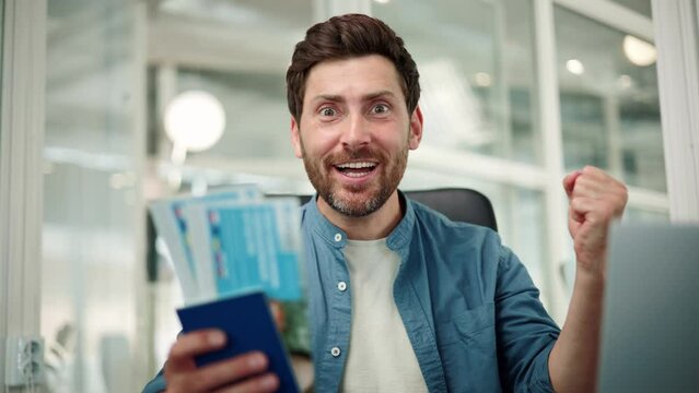 Happy excited office worker holds a passport with vacation tickets, looks into the camera, and enthusiastically shouts wow, last day of work in the office before going on vacation with their family.
