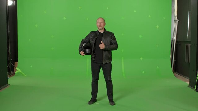 Man with black full Face Motorcycle Helmet standing and raising thumb up on green screen chroma key background. People, modern lifestyle and youth concept.