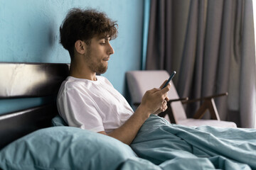 Handsome young man using phone in bed after waking up in the morning