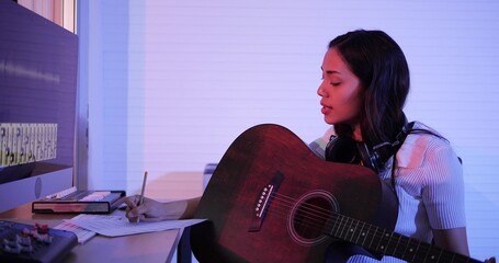 Happy young asian woman songwriter play acoustic guitar think and write notes lyrics song in paper....