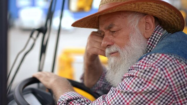 Close-up tired male senior farmer thinking sitting in tractor cabin. Side view closeup portrait of overworked Caucasian man in agricultural harvester outdoors