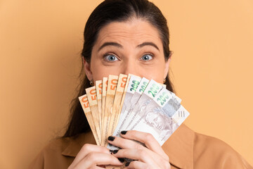 happy mature woman with money, brazilian real in beige background. 