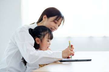 Obraz na płótnie Canvas リビングにてペンとタブレットを使用して勉強をする日本人の親娘
