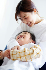 ソファーの上で元気よく遊ぶ幸せそうな日本人の母親と子供