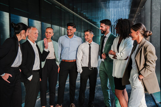 Executive businesspeople talking, having a relaxed conversation with their colleagues, taking a break in the office workplace. Group of business men and women in formalwear on a brainstorming reunion