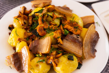 baked potatoes with chanterelles and bacon served with herbs on white plate