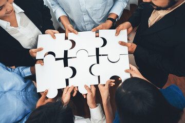 Diverse corporate officer workers collaborate in office, connecting puzzle pieces to represent partnership and teamwork. Unity and synergy in business concept by merging jigsaw puzzle. Concord - obrazy, fototapety, plakaty
