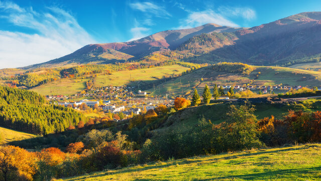 rural area of carpathian mountains in autumn. village in the distant valley. trees on the hills in fall colors. distant mountain ridge beneath a sky with clouds
