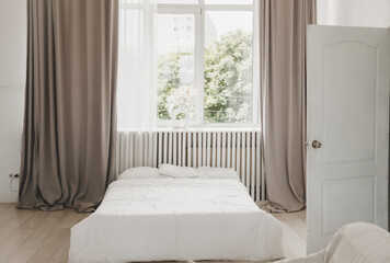 Interior of a white bedroom with curtains and white pillows on a wooden bed, a classic for relaxing...