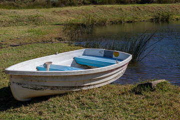 A small white colored wooden row boat on the green grass next to a lake